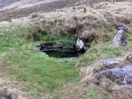 Small stone lined Krosslaug hot pool set into a grassy slope in Lundarreykjadalur