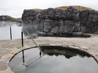 Round cold plunge pool on stone paving beside the Sky Lagoon and its rocky cliff wall