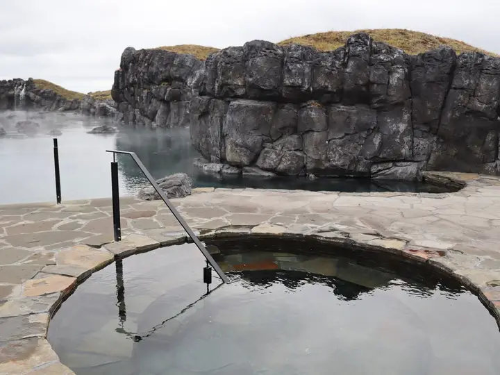 Round cold plunge pool on stone paving beside the Sky Lagoon and its rocky cliff wall