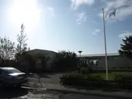 Entrance to the Vesturbæjarlaug pool building with a flagpole, shrubs and trees in west Reykjavík