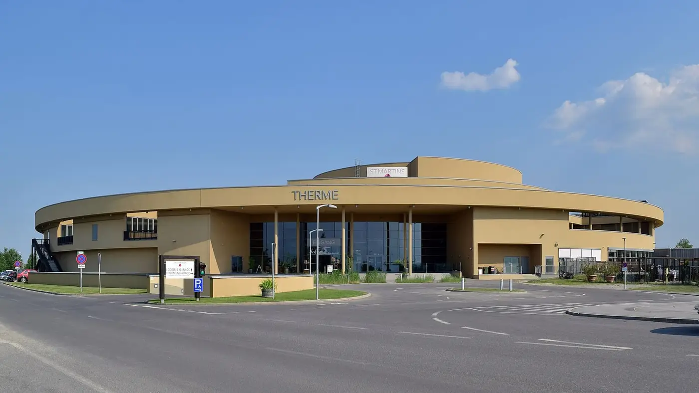 Curved sand colored main building of St. Martins Therme in Frauenkirchen under a blue sky