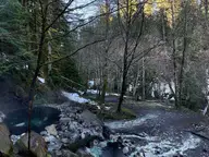 Steaming rock and mud pool beside Boulder Creek at Olympic Hot Springs in a snowy winter forest