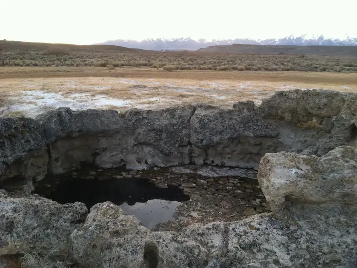 Shallow water inside the rough sinter collar of the Paradise Valley hot spring with snowy Santa Rosa Mountains beyond
