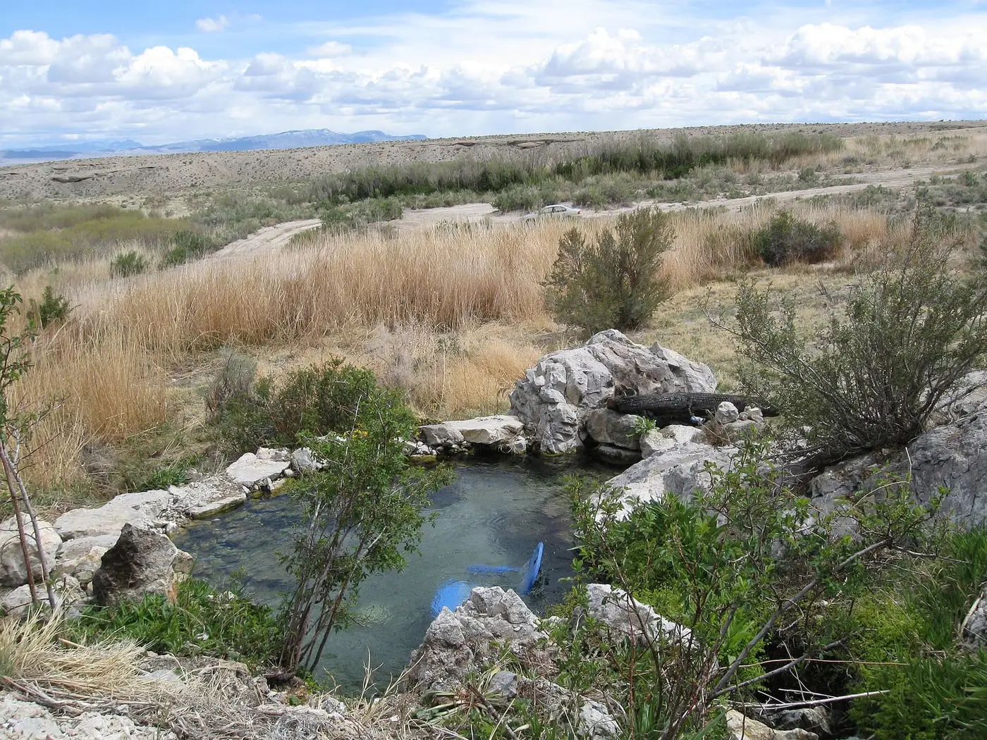 Clear rock rimmed pool at Gandy Warm Springs in open desert grassland with distant mountains