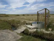 Metal stock tank tub with wooden fence and plank deck beside a small hot water channel near Double Hot Springs