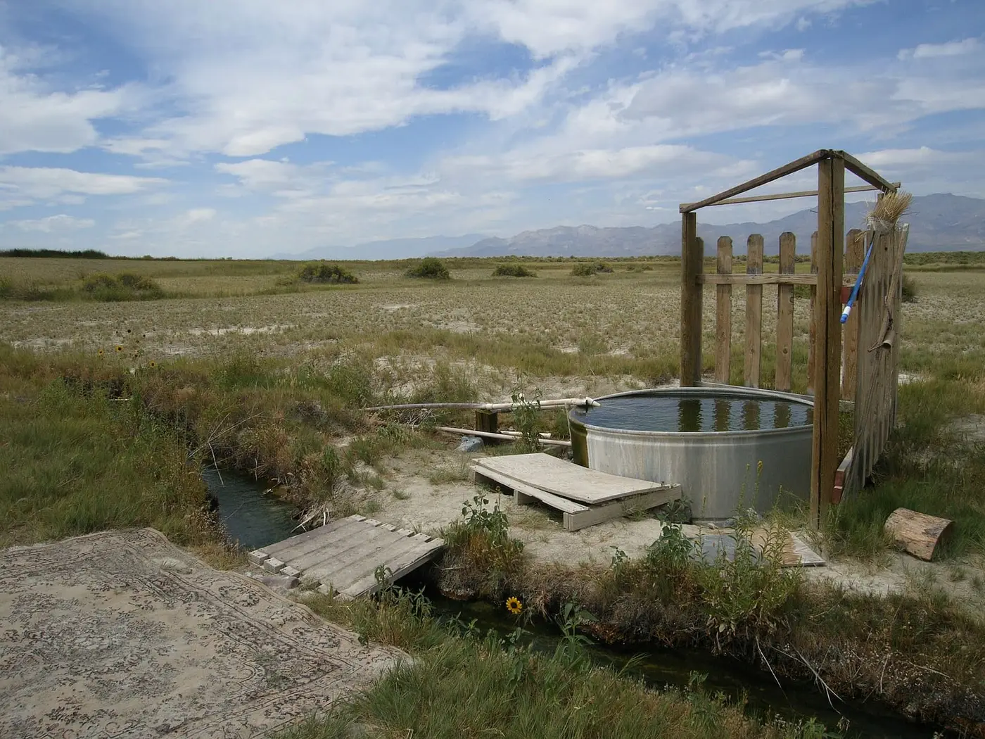 Metal stock tank tub with wooden fence and plank deck beside a small hot water channel near Double Hot Springs