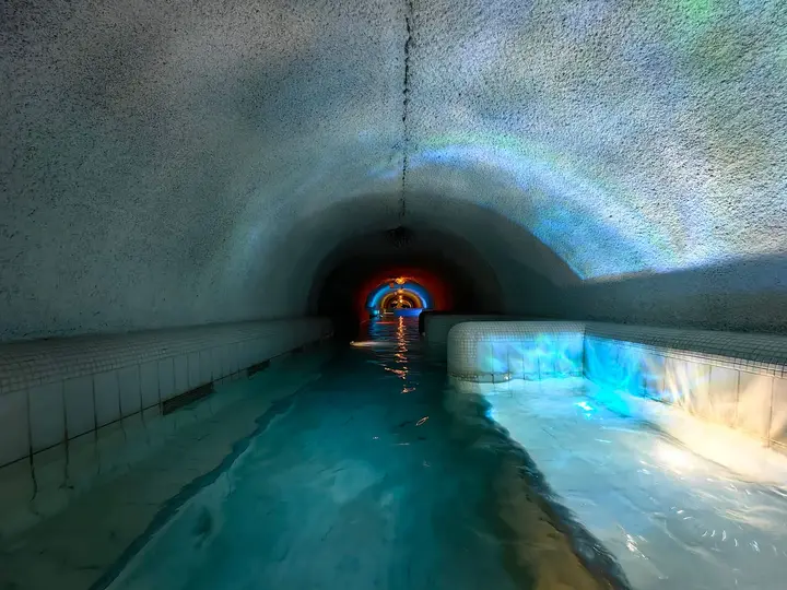 Turquoise thermal water flowing through a rough white rock tunnel in the Demjén Cascade cave bath