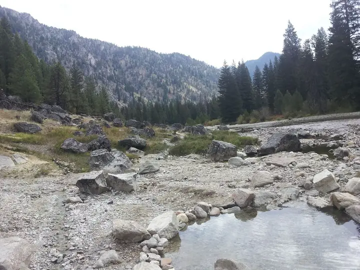Rock lined soaking pool at Sacajawea Hot Springs below forested mountains along the South Fork Payette