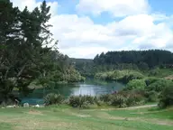Grassy bank of Spa Thermal Park above the Waikato River with forested hills beyond