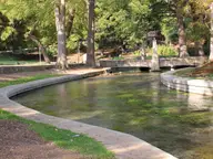 Clear spring fed Comal River channel and stone footbridge under shade trees in Landa Park