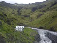 Seljavallalaug pool and white changing house beside a rushing river in a steep green valley