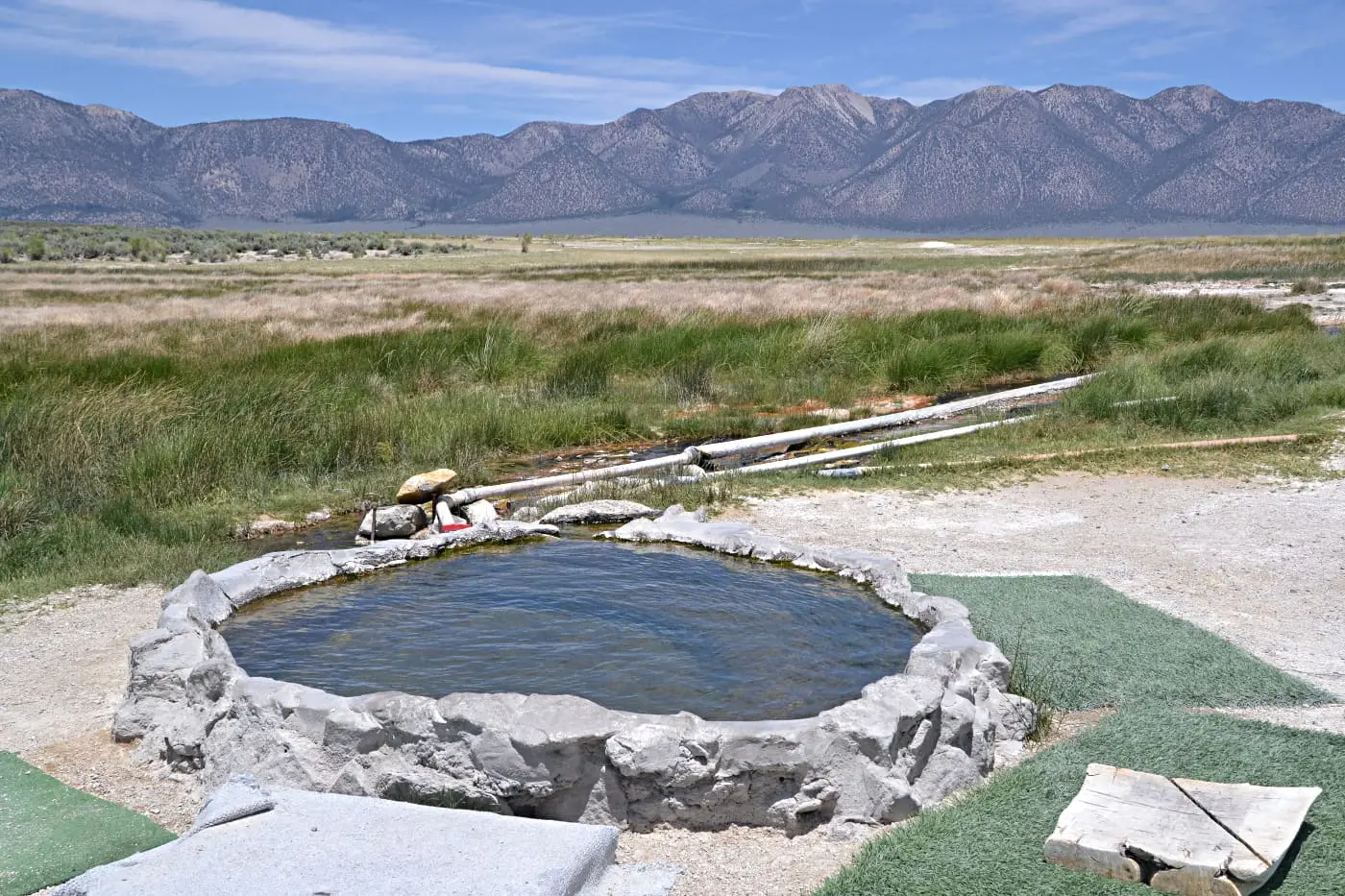 Round rock and cement soaking tub at Hilltop Hot Springs in Long Valley with the Glass Mountains beyond