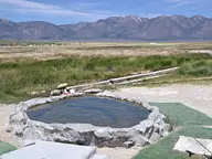 Round rock and cement soaking tub at Hilltop Hot Springs in Long Valley with the Glass Mountains beyond