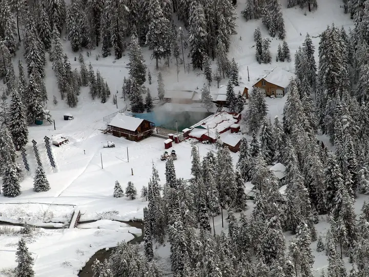 Silver Creek Plunge in winter, its steaming pool among snowy cabins and fir forest