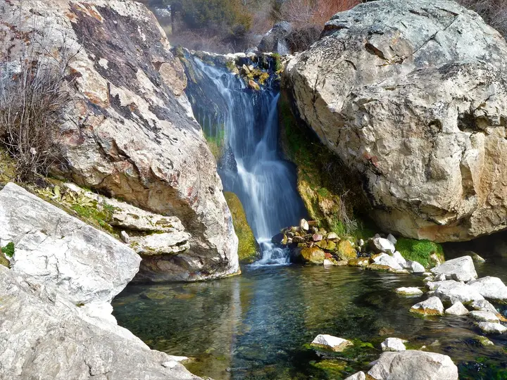 Waterfall pouring between large boulders into a clear rock-lined pool at Goldbug Hot Springs