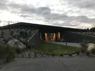 Low modern entrance building of Opuke Thermal Pools with a lit doorway and native plantings at dusk