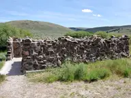 Stone walls enclosing the Hart Mountain Hot Springs bathing pool beside a gravel path and rolling hills