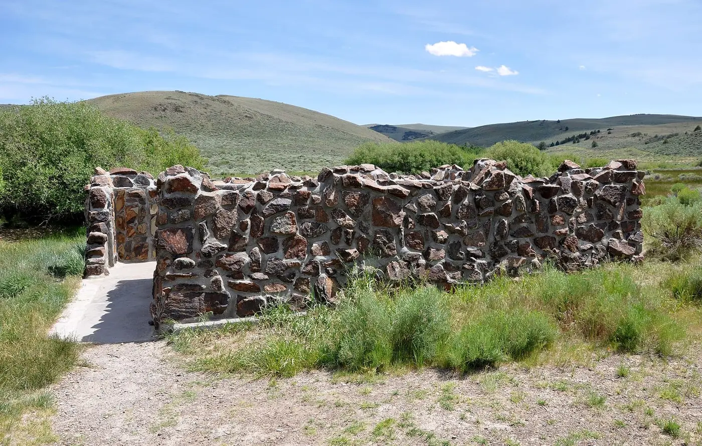 Stone walls enclosing the Hart Mountain Hot Springs bathing pool beside a gravel path and rolling hills