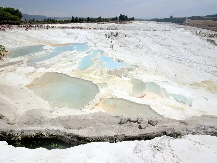 Pale blue thermal pools on the white travertine terraces of Pamukkale under a hazy sky