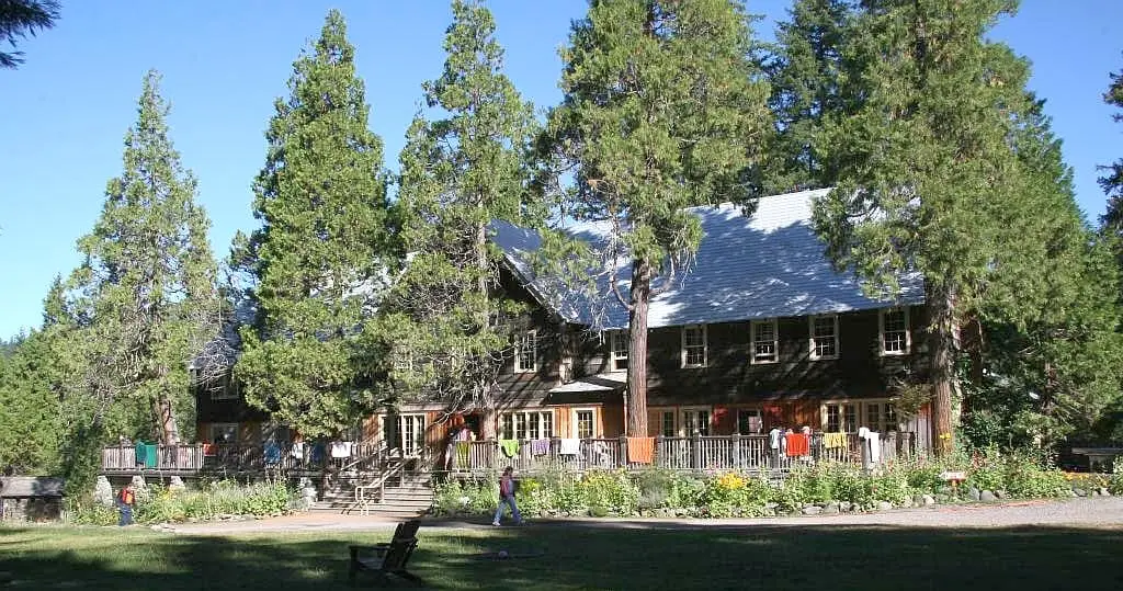 Main lodge at Breitenbush Hot Springs behind tall conifers and a sunny front lawn