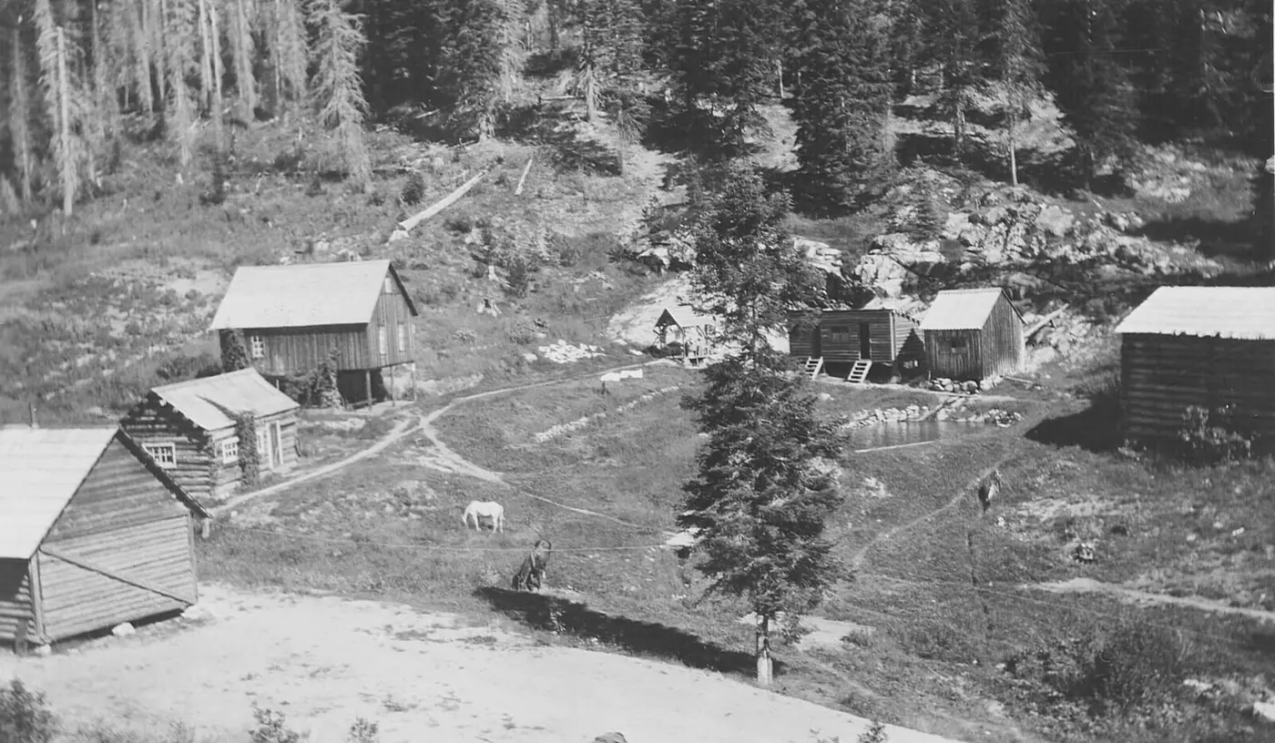 Historic photo of log cabins and a small pool at Red River Hot Springs in a forested clearing