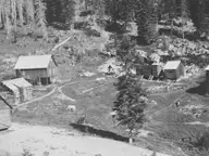 Historic photo of log cabins and a small pool at Red River Hot Springs in a forested clearing