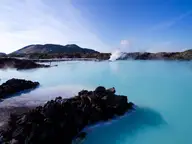 Steaming milky blue water of the Blue Lagoon framed by black lava rocks and hills