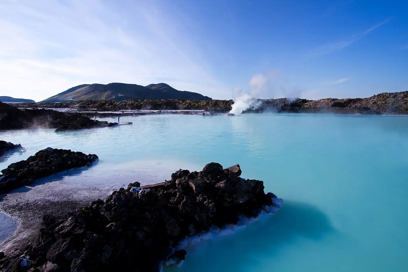 Steaming milky blue water of the Blue Lagoon framed by black lava rocks and hills