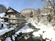 Wooden Osenkaku inn beside the snowy Takaragawa river gorge under blue sky