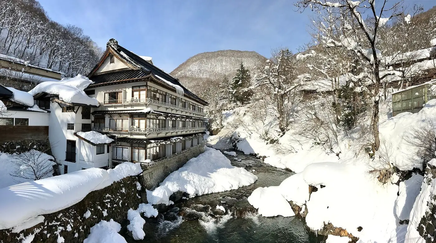 Wooden Osenkaku inn beside the snowy Takaragawa river gorge under blue sky