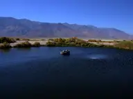 Dark blue pool of Dirty Socks Hot Spring with a concrete wellhead, desert brush and bare mountains beyond