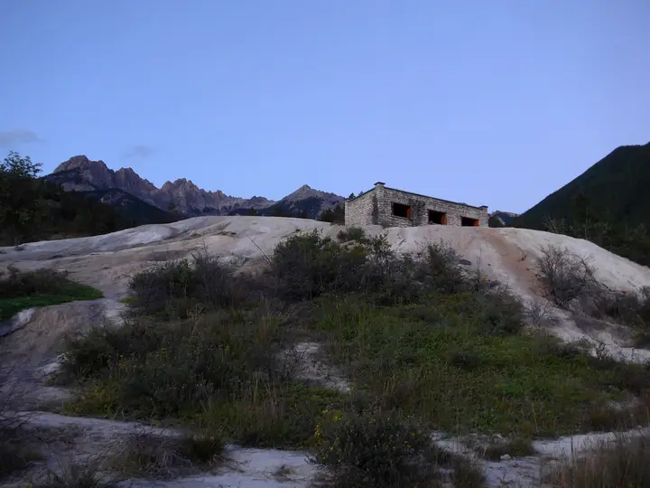 Historic stone bath building on a pale mineral mound at Fairmont Hot Springs with mountains behind
