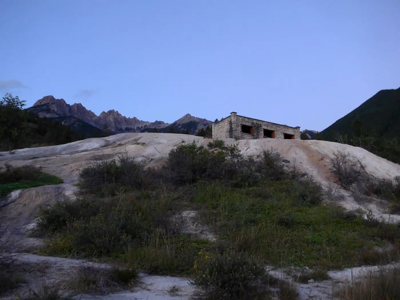 Historic stone bath building on a pale mineral mound at Fairmont Hot Springs with mountains behind