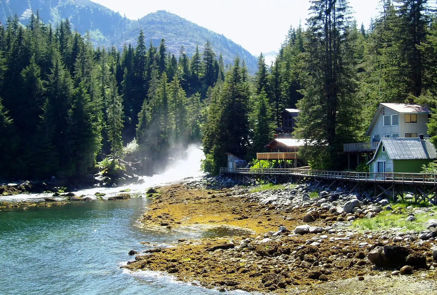 Houses on a boardwalk beside a rushing waterfall and rocky tidal shore at Baranof Warm Springs