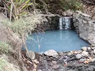 Small rock walled pool of milky blue water at Gaviota Hot Springs, fed by a trickling cascade
