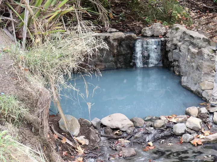 Small rock walled pool of milky blue water at Gaviota Hot Springs, fed by a trickling cascade