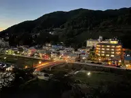 Shibu Onsen village at dusk with lit inns and a bridge below forested mountains