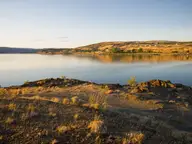 Calm waters of Soap Lake at golden hour seen from its rocky, grassy south shore