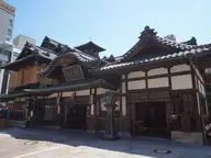 Wooden multi roofed facade of Dogo Onsen Honkan bathhouse under a clear blue sky