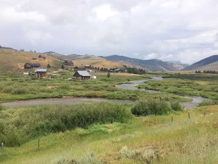 Creek winding through green meadows below the houses of Stanley, Idaho, under a cloudy sky