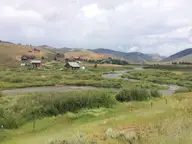 Creek winding through green meadows below the houses of Stanley, Idaho, under a cloudy sky