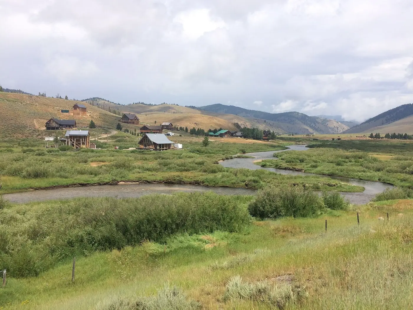 Creek winding through green meadows below the houses of Stanley, Idaho, under a cloudy sky