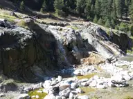 Hot water spilling over mineral crusted rock terraces at Bonneville Hot Springs below pine forest