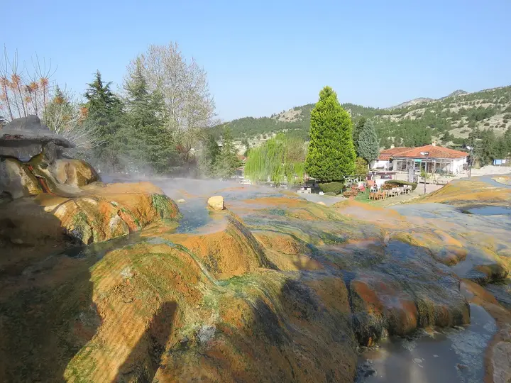 Steaming orange and red travertine at the Karahayıt Red Spring with houses and pines behind