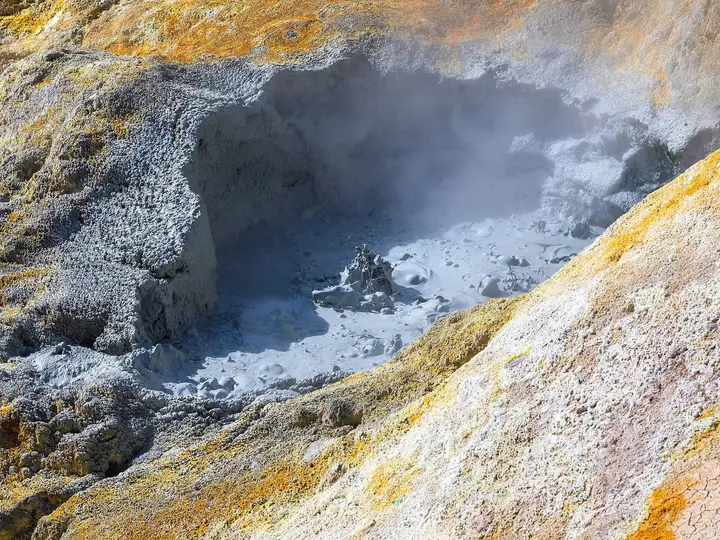 Gray bubbling mudpot ringed by yellow and orange mineral deposits at Sulphur Works in Lassen Volcanic National Park
