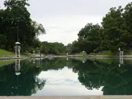 Still green water of Barton Springs Pool reflecting trees and lifeguard stands on a calm day