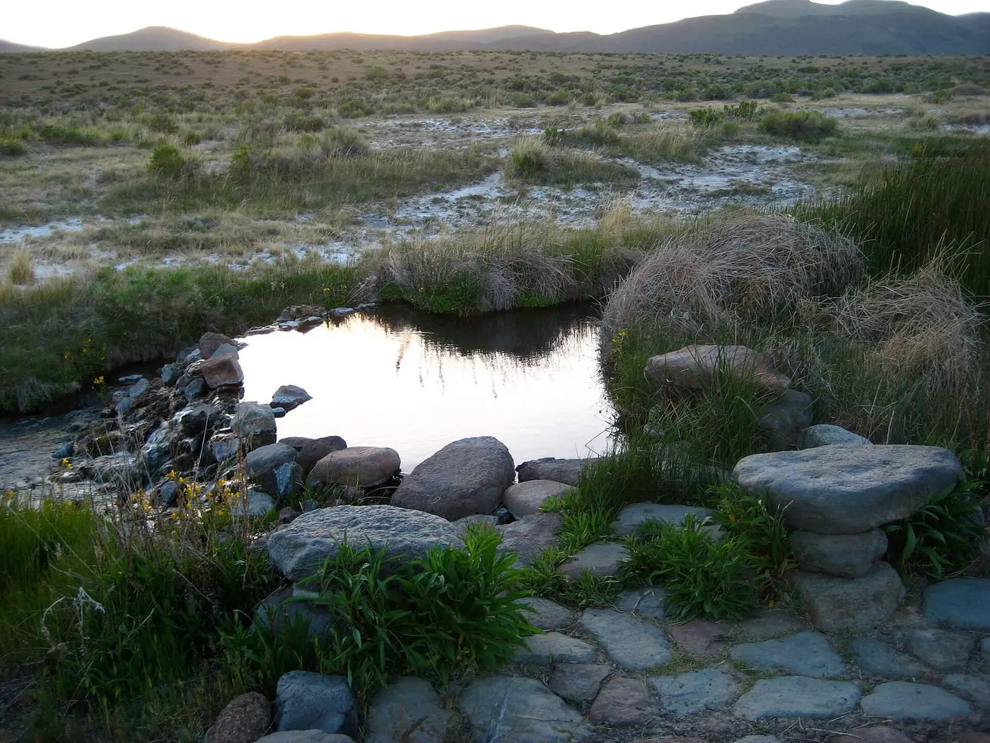 Rock rimmed soaking pool among grasses and sagebrush at Soldier Meadows Hot Springs under low evening light