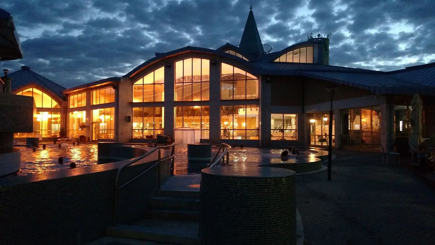 Sárvár spa building lit up at dusk with outdoor thermal pools in front