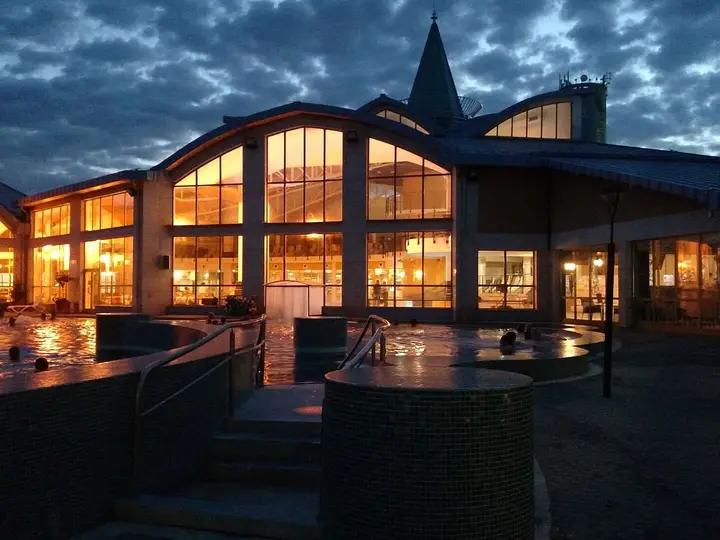 Sárvár spa building lit up at dusk with outdoor thermal pools in front