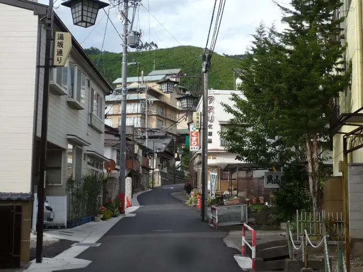 Narrow street climbing through Asama Onsen town past inns toward green hills in Matsumoto